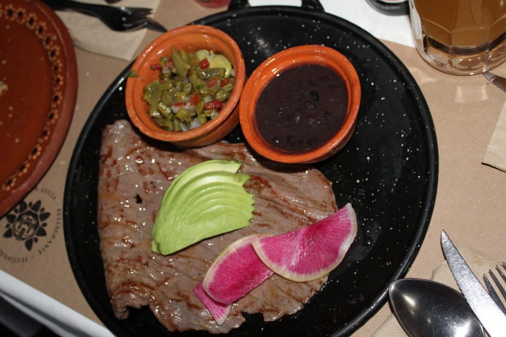 Cured beef with avocado, beans, cactus salad etc. on a plate.